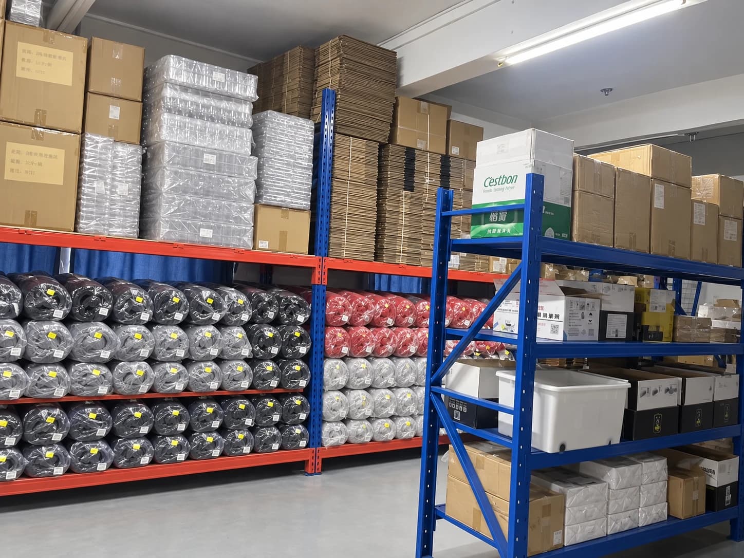 Storage racks holding wrapped fabric rolls, flattened cartons, and packaging supplies